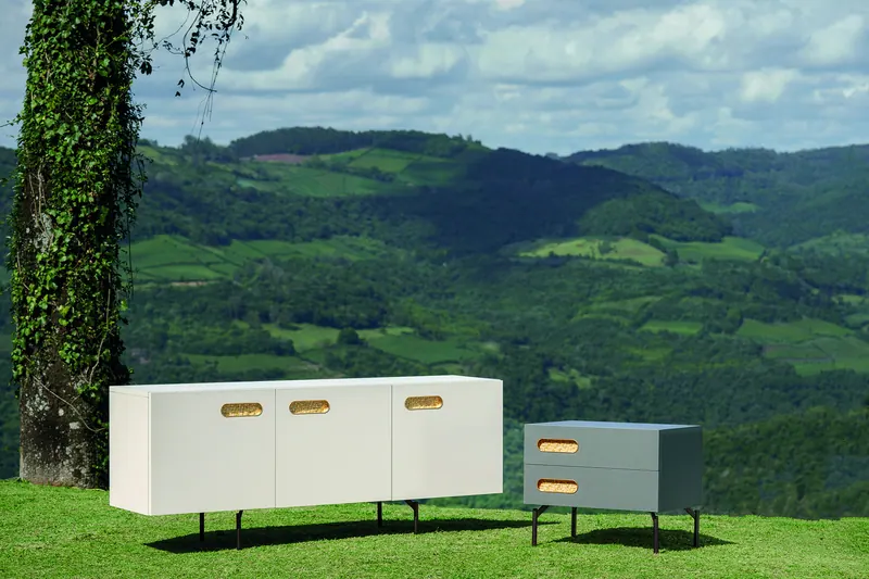 Buffet claro e mesa de cabeceira cinza com gavetas, fotografados em gramado com vista