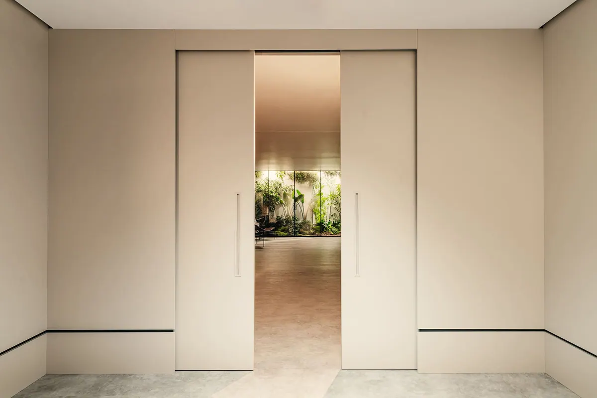 Portas de correr embutidas em tom claro entreabertas, com jardim visível ao fundo