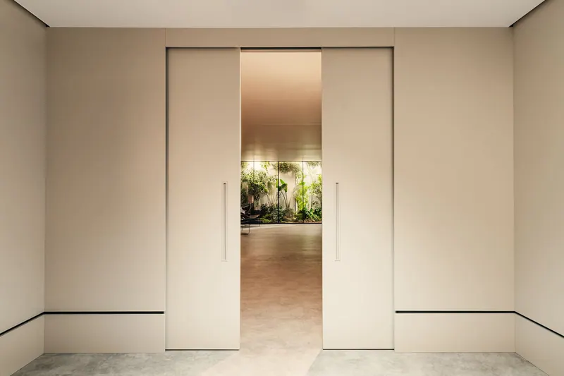 Portas de correr embutidas em tom claro entreabertas, com jardim visível ao fundo