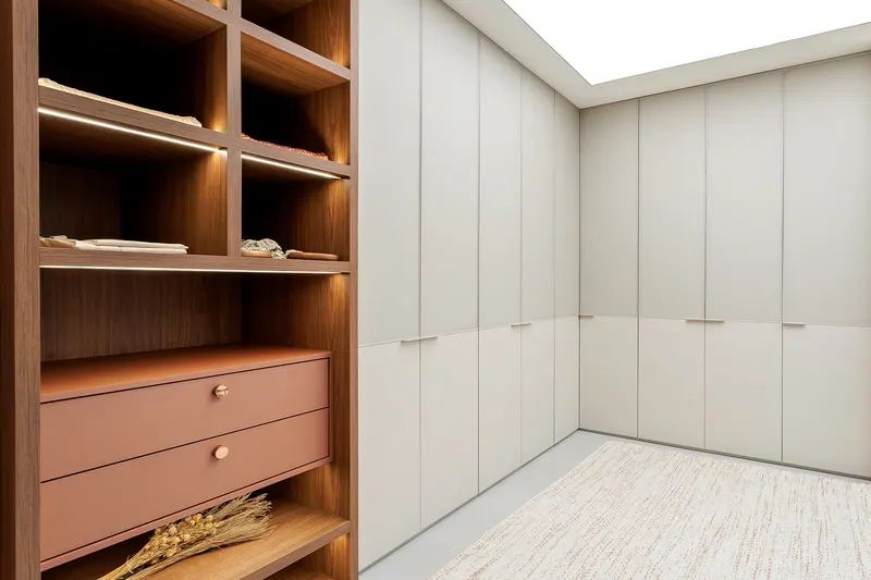 Closet com armários de portas lisas claras, nichos amadeirados iluminados e gavetas em tom terracota