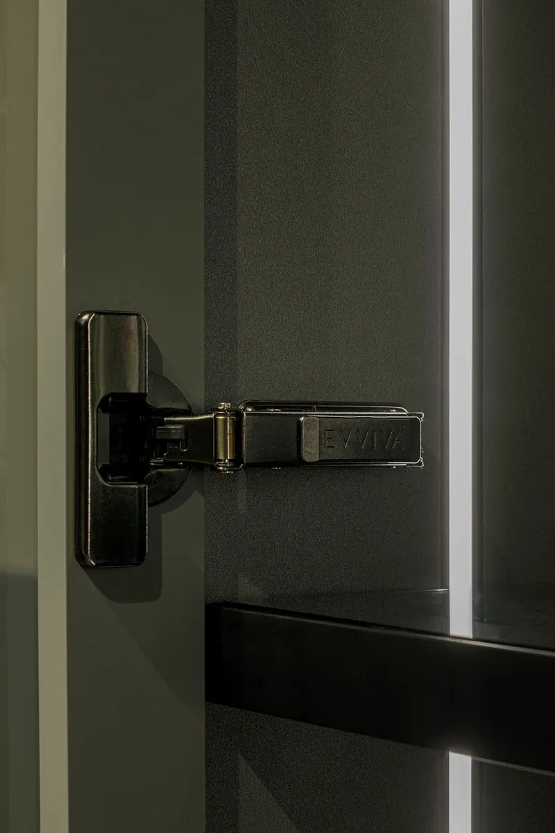 Close de dobradiça metálica escura em porta de armário com perfil de led