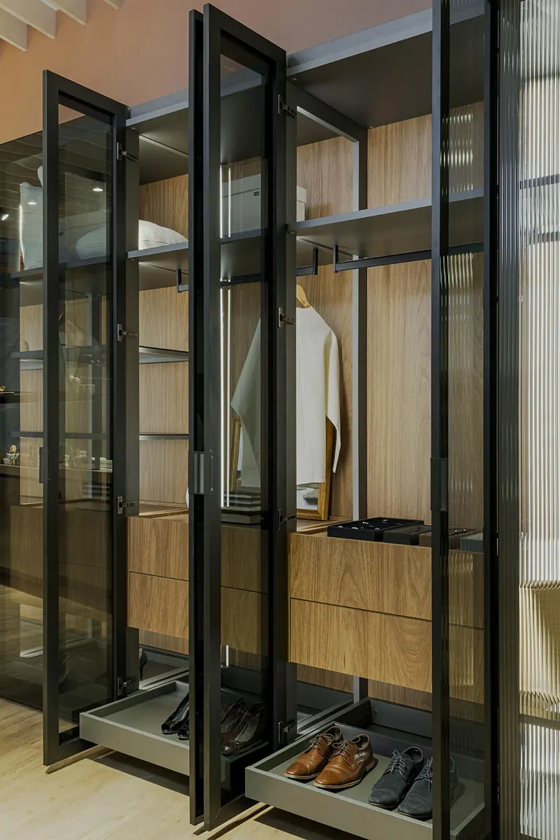 Armário de closet com portas de vidro abertas, gavetas amadeiradas e sapateiras deslizantes