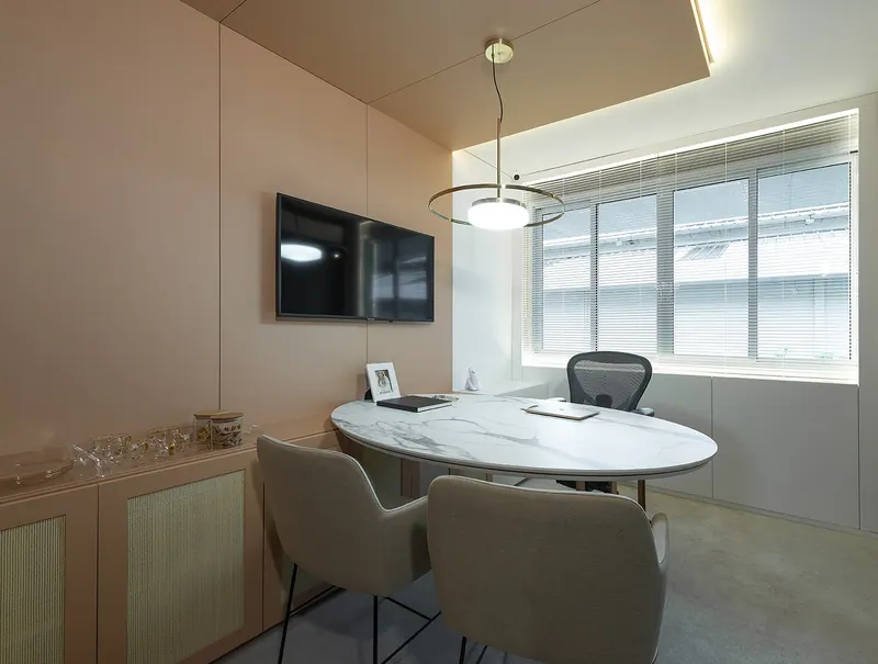 Sala de reunião com painéis em tom nude, armário baixo com portas de palhinha e mesa oval