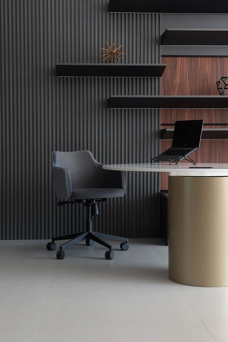 Escritório com painel ripado escuro, prateleiras, fundo amadeirado e mesa com base cilíndrica