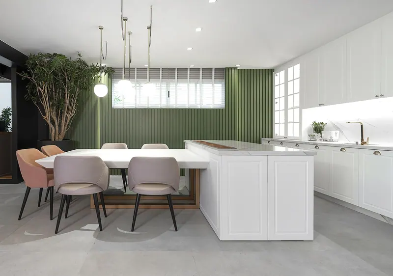 Cozinha com armários brancos almofadados até o teto, ilha com mesa acoplada e painel ripado verde