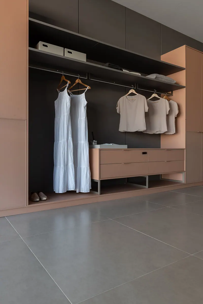 Closet aberto em tom escuro com cabideiros, prateleiras e gaveteiro em tom terracota