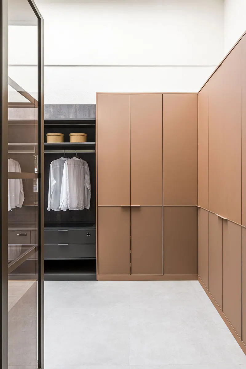 Closet com armários de portas lisas em tom terracota e módulo aberto escuro com cabideiro