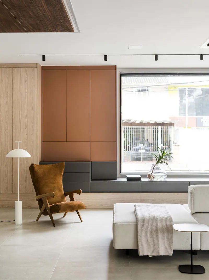 Sala com armário superior em tom terracota, painel amadeirado claro e banco baixo escuro sob a janela