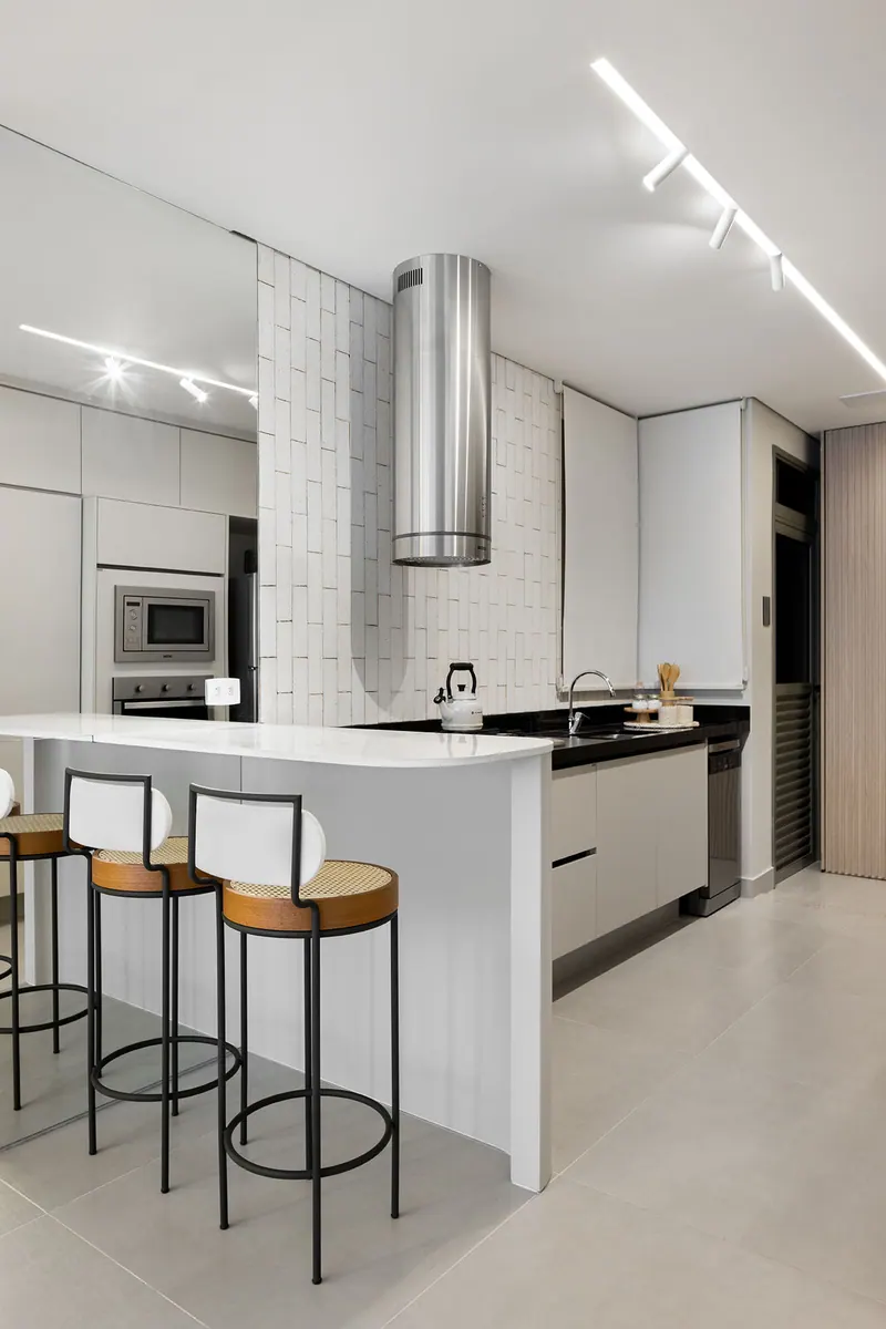 Cozinha branca com península e banquetas, armários superiores, torre de fornos e coifa cilíndrica em inox