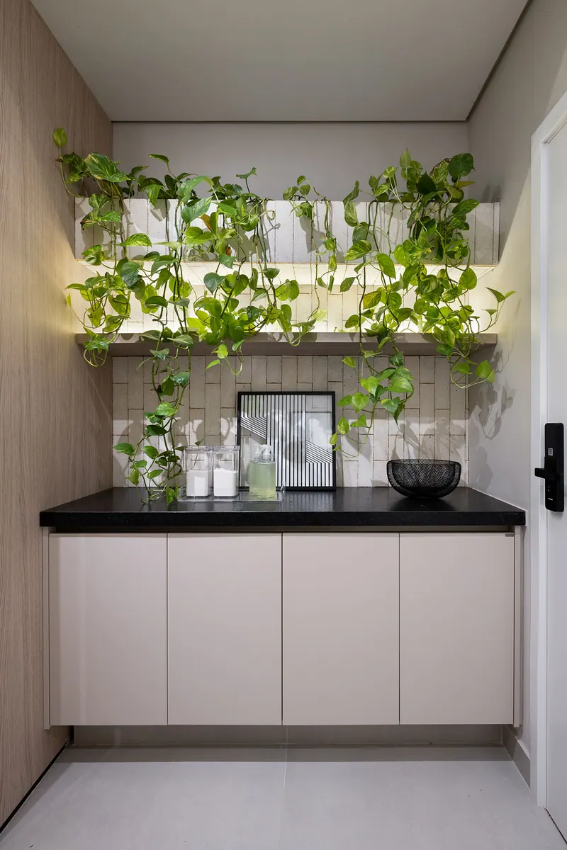 Bancada preta com armários inferiores claros, prateleiras com led e plantas, e painel lateral em tom amadeirado