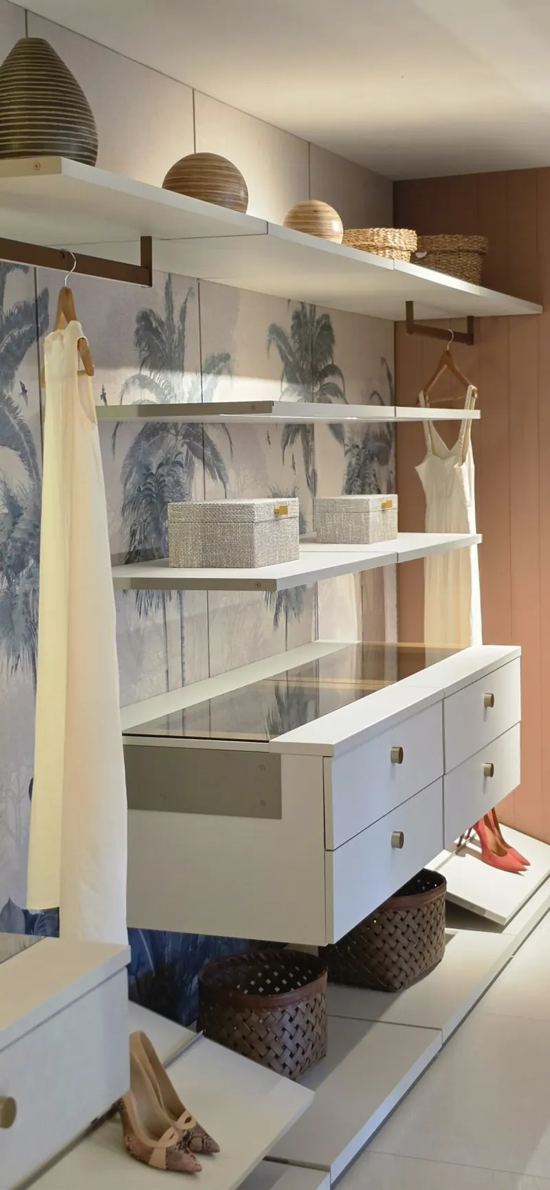 Closet de exposição com prateleiras claras, gaveteiro suspenso com tampo de vidro e sapateira inclinada