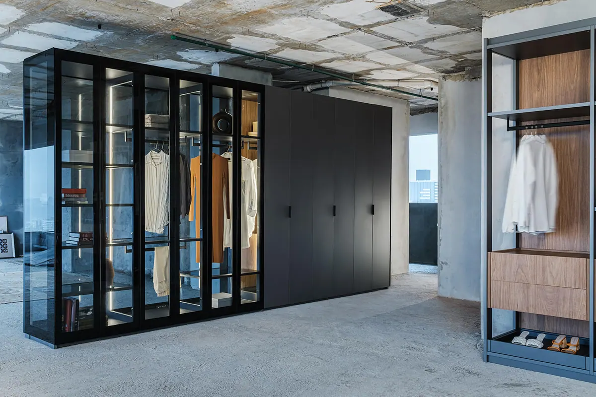 Guarda-roupa com portas de vidro e interior iluminado ao lado de módulo de portas escuras