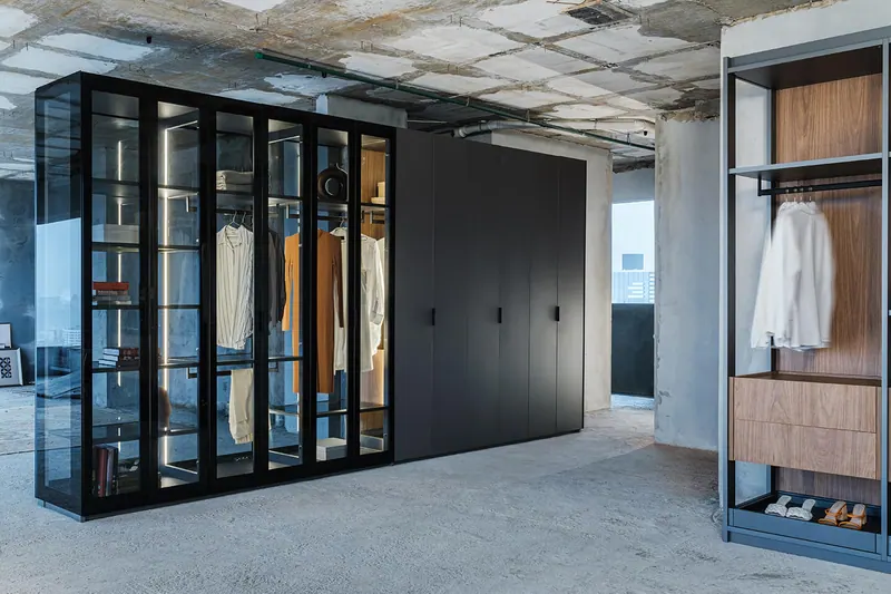 Guarda-roupa com portas de vidro e interior iluminado ao lado de módulo de portas escuras