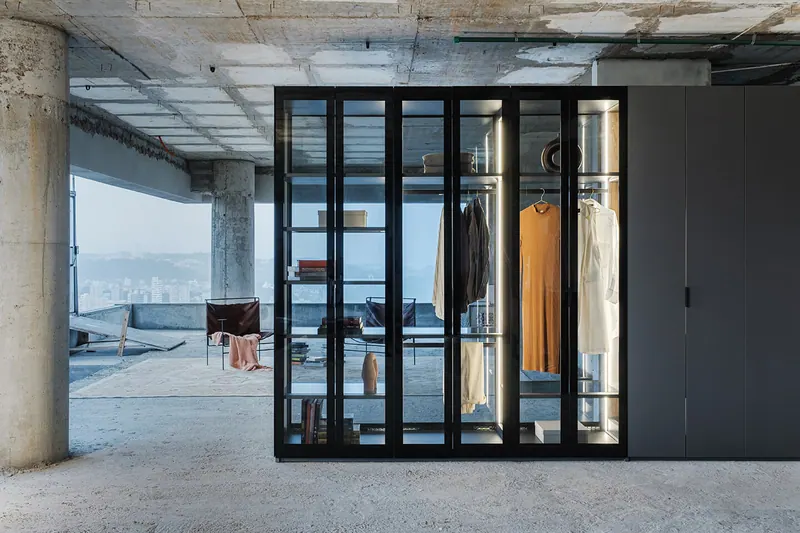 Guarda-roupa com portas de vidro, cabideiro e prateleiras iluminadas em pavimento de concreto aparente