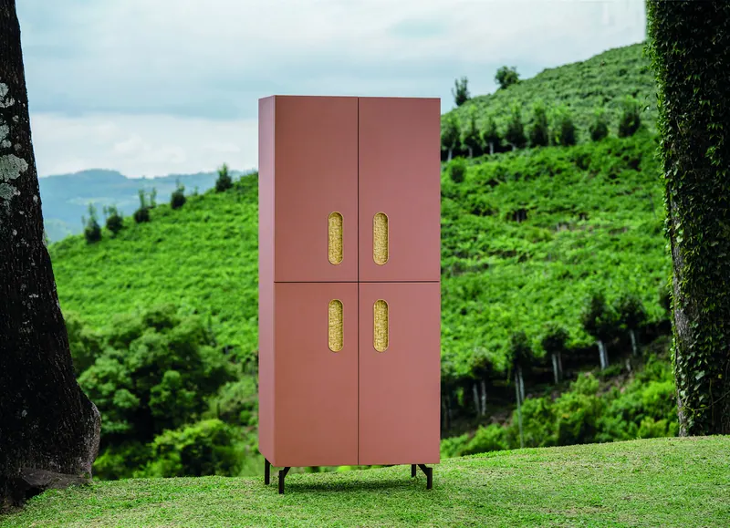 Armário alto rosado de quatro portas com puxadores recortados, fotografado em paisagem verde