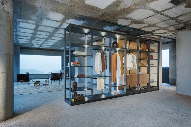 Closet aberto em estrutura metálica com prateleiras, cabideiros e gavetas, em pavimento de concreto aparente