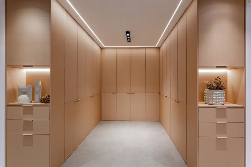 Closet em corredor com armários até o teto em tom claro, gavetas e nichos iluminados
