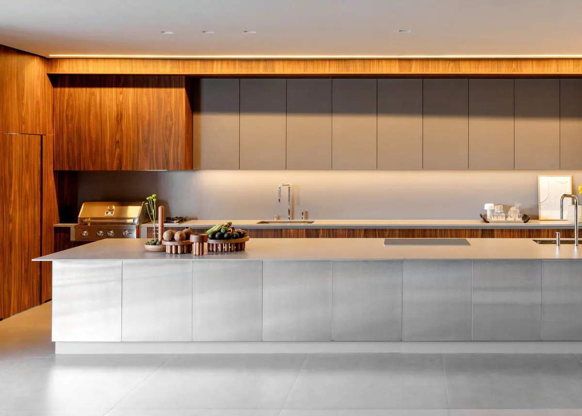 Cozinha com ilha em inox, armários superiores cinza, painel em tom amadeirado e led embutido