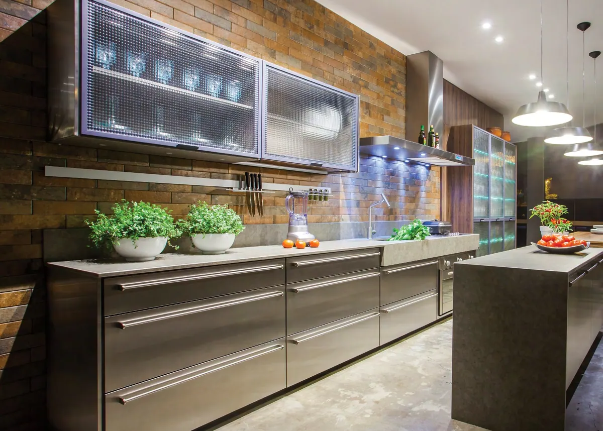 Cozinha linear com gavetões em inox, aéreos de vidro texturizado e ilha com tampo de pedra