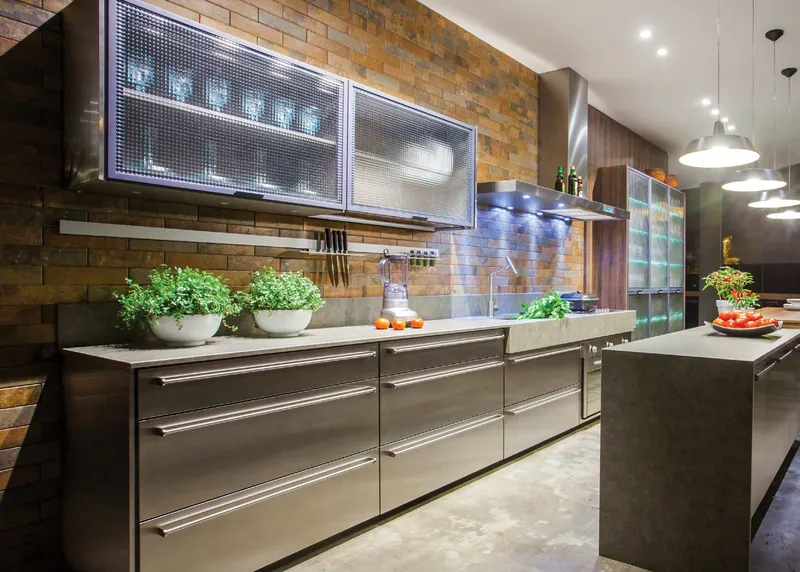 Cozinha linear com gavetões em inox, aéreos de vidro texturizado e ilha com tampo de pedra