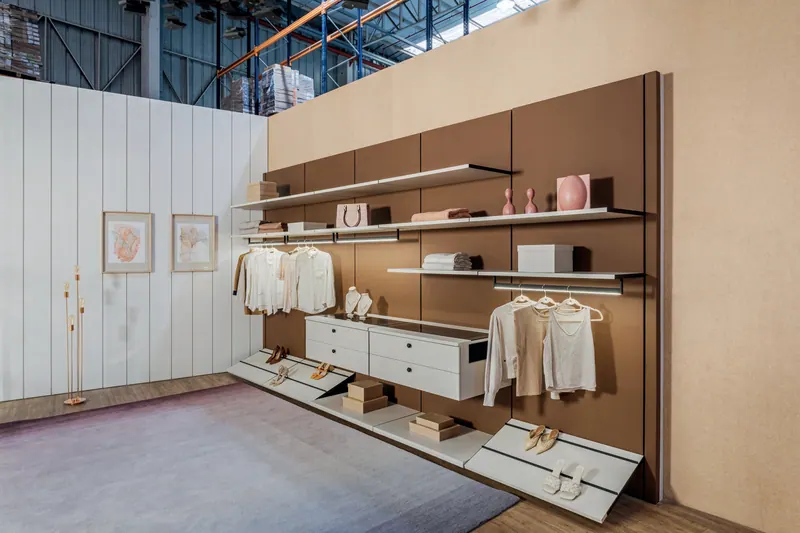 Closet aberto com painel em tom marrom, prateleiras, cabideiros, gaveteiro branco e sapateiras inclinadas