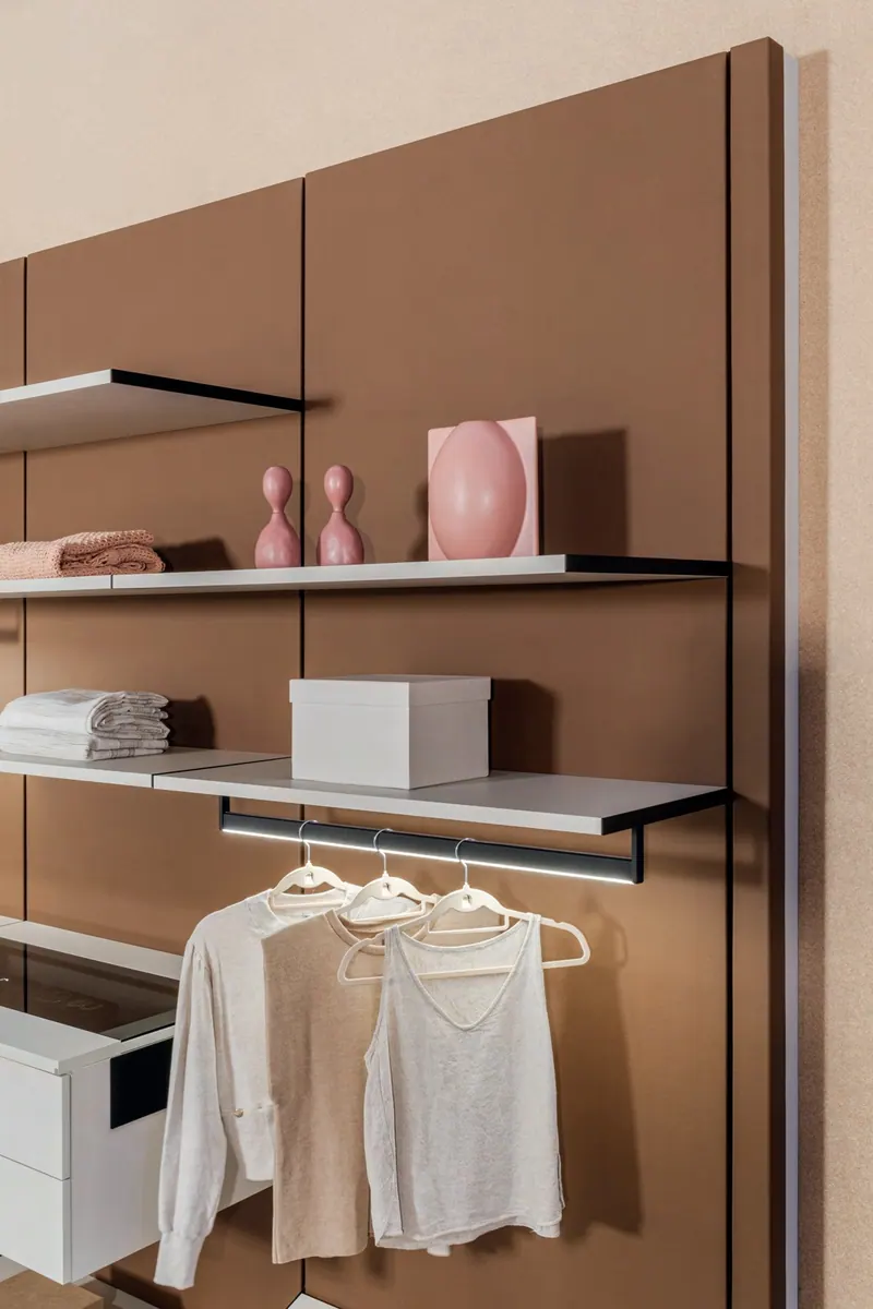 Trecho de closet aberto com painel marrom, prateleiras finas, cabideiro e gaveta branca
