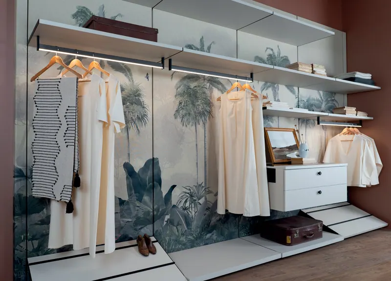 Closet aberto com prateleiras brancas, cabideiros iluminados, gaveteiro suspenso e sapateira inclinada