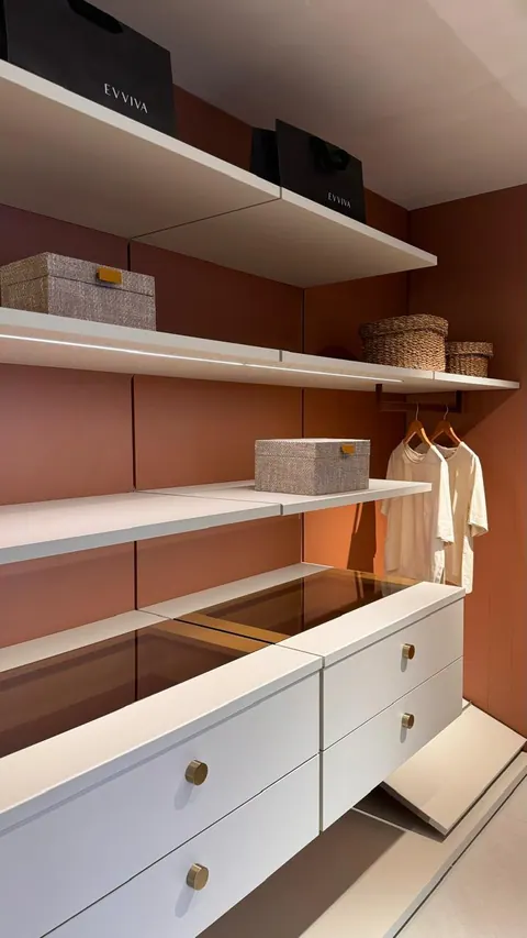 Closet aberto com painel terracota, prateleiras claras com led, cabideiro e gaveteiro com tampo de vidro