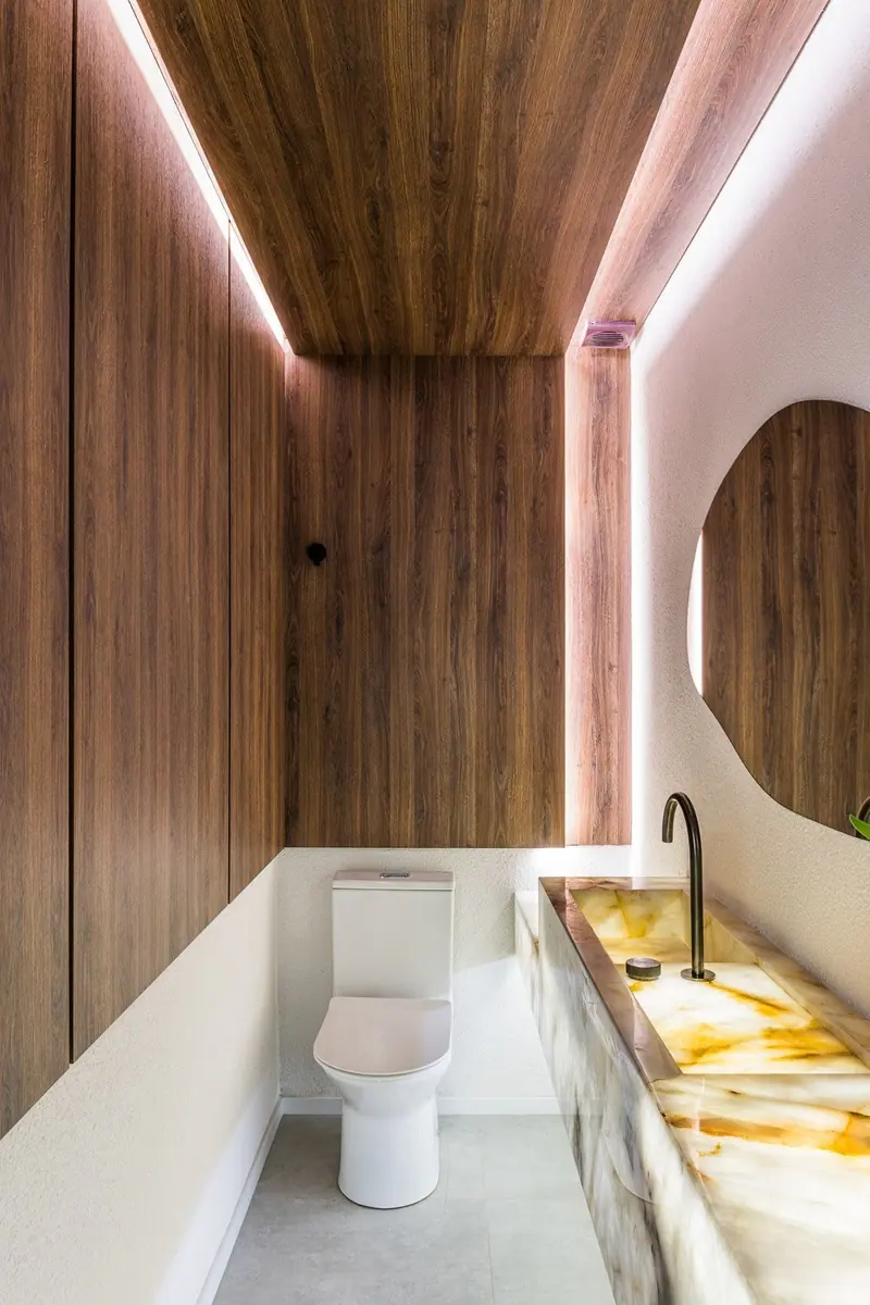 Lavabo com painel e forro em tom amadeirado e bancada iluminada